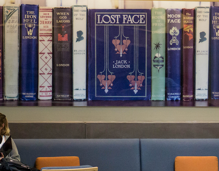 two students talk below a large wall art of spines of Jack London books