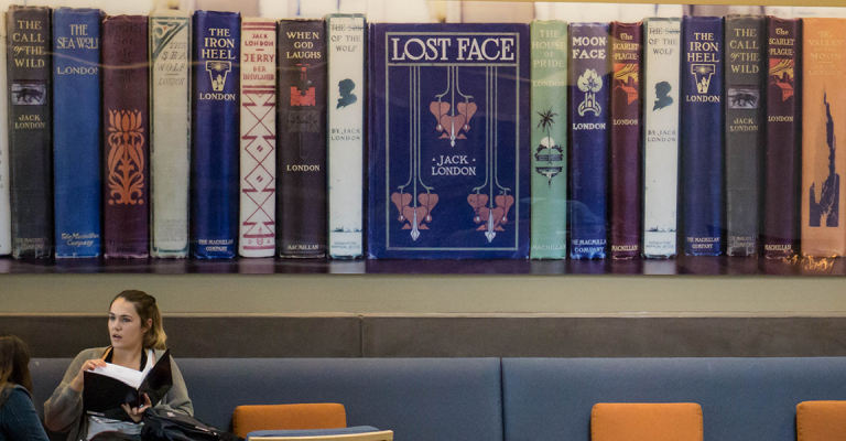 two students talk below a large wall art of spines of Jack London books